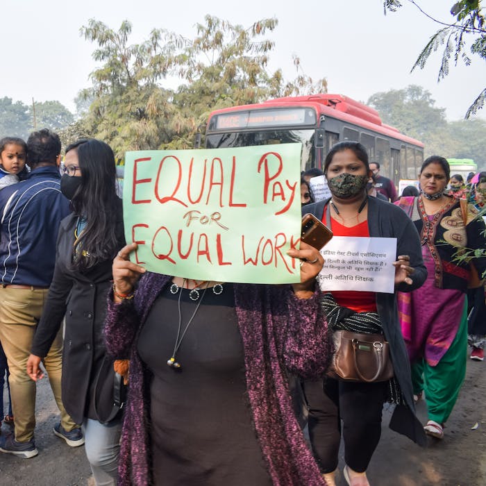 Women protesting for equal pay, holding signs in an outdoor rally.